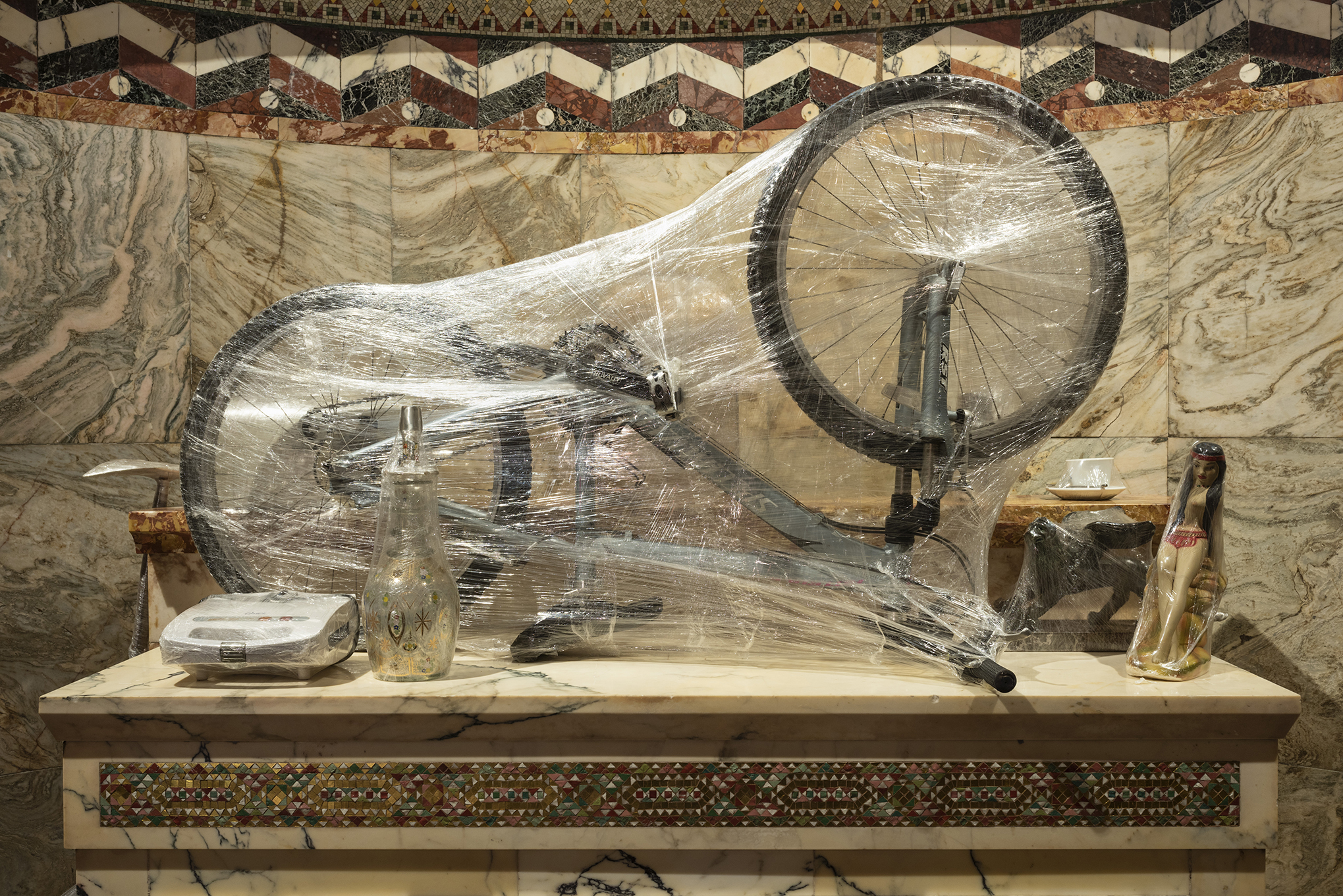 Crisálida, wrapped bicycle and objects on marble shelf